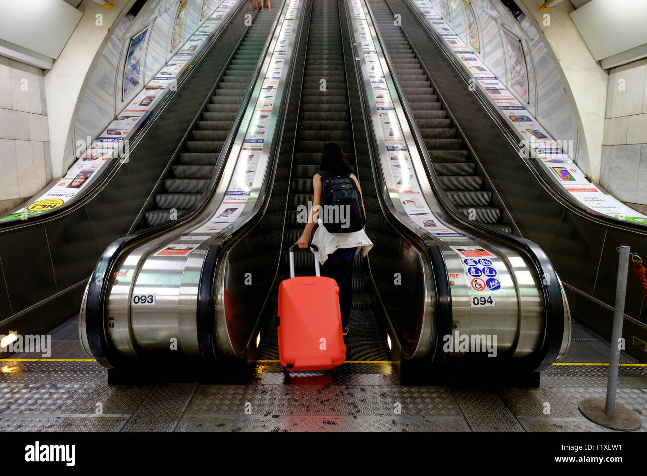 Rückansicht einer Person mit einem roten rollenden Koffer auf einer Rolltreppe hinauf Stockfoto