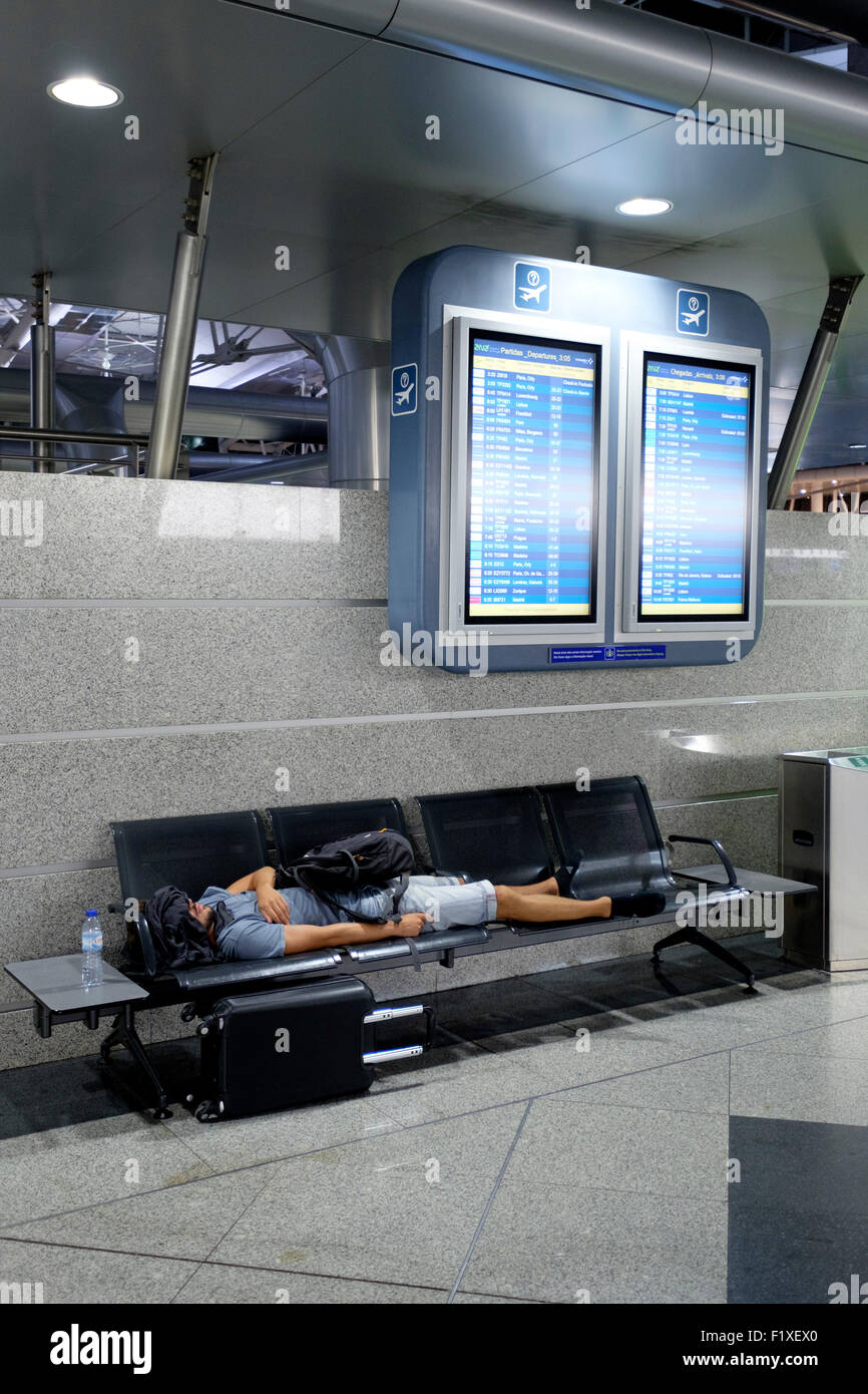 Passagier schlafen auf einer Bank unter zwei Flug-Zeitplan-Boards am Sá Carneiro Airport terminal in Porto, Portugal Stockfoto