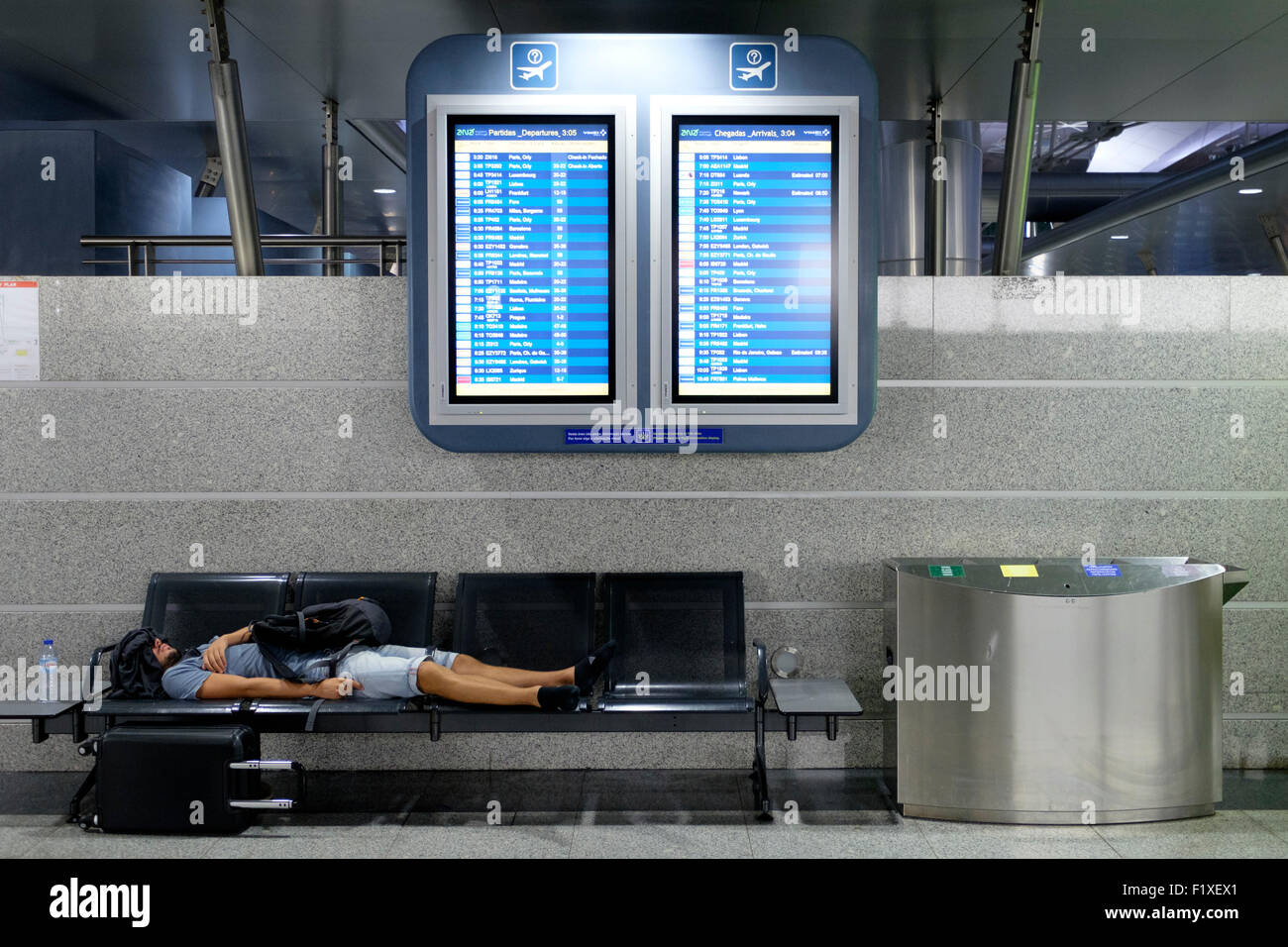 Passagier schlafen auf einer Bank unter zwei Flug-Zeitplan-Boards am Sá Carneiro Airport terminal in Porto, Portugal Stockfoto