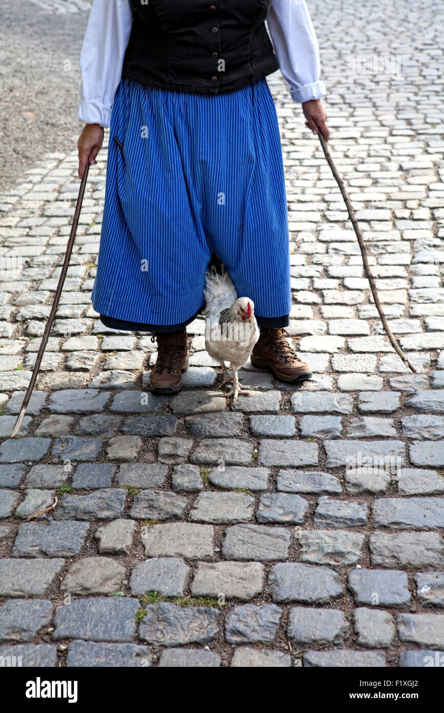 Ein Huhn wird von einer mittelalterlichen gekleidete Frauen mit Stöcken auf einem gepflasterten Weg, Deutschland geführt, Stockfoto