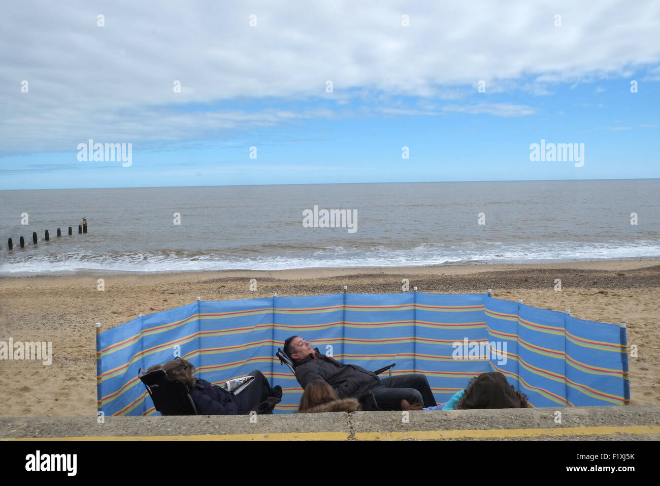 komische Tag am Meer zeigt Familie entspannende hinter einem Windschutz Stockfoto