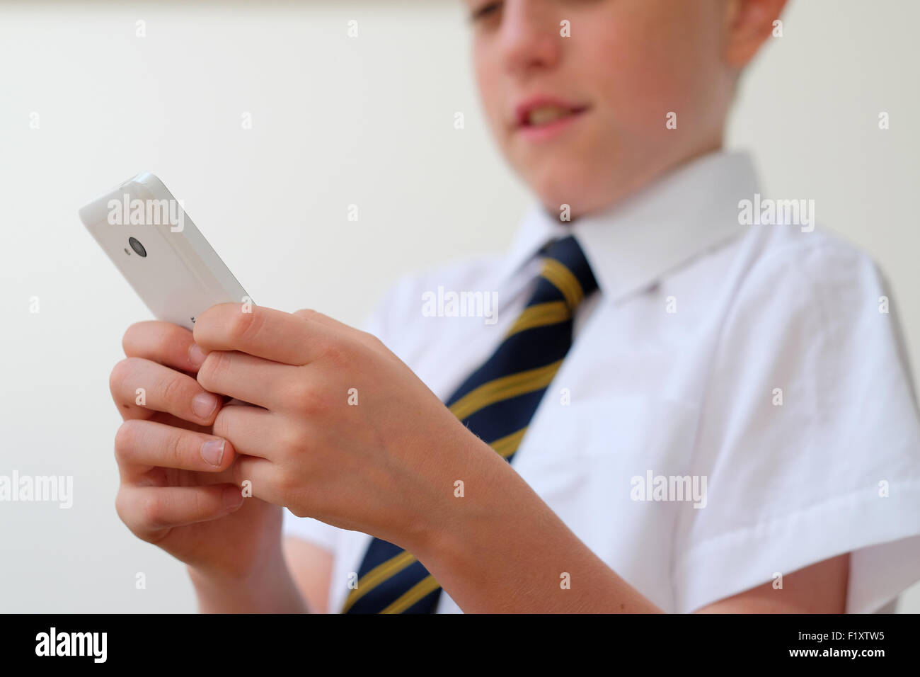 Ein Schulkind in Uniform mit seinem Mobiltelefon (SMS) UK Stockfoto