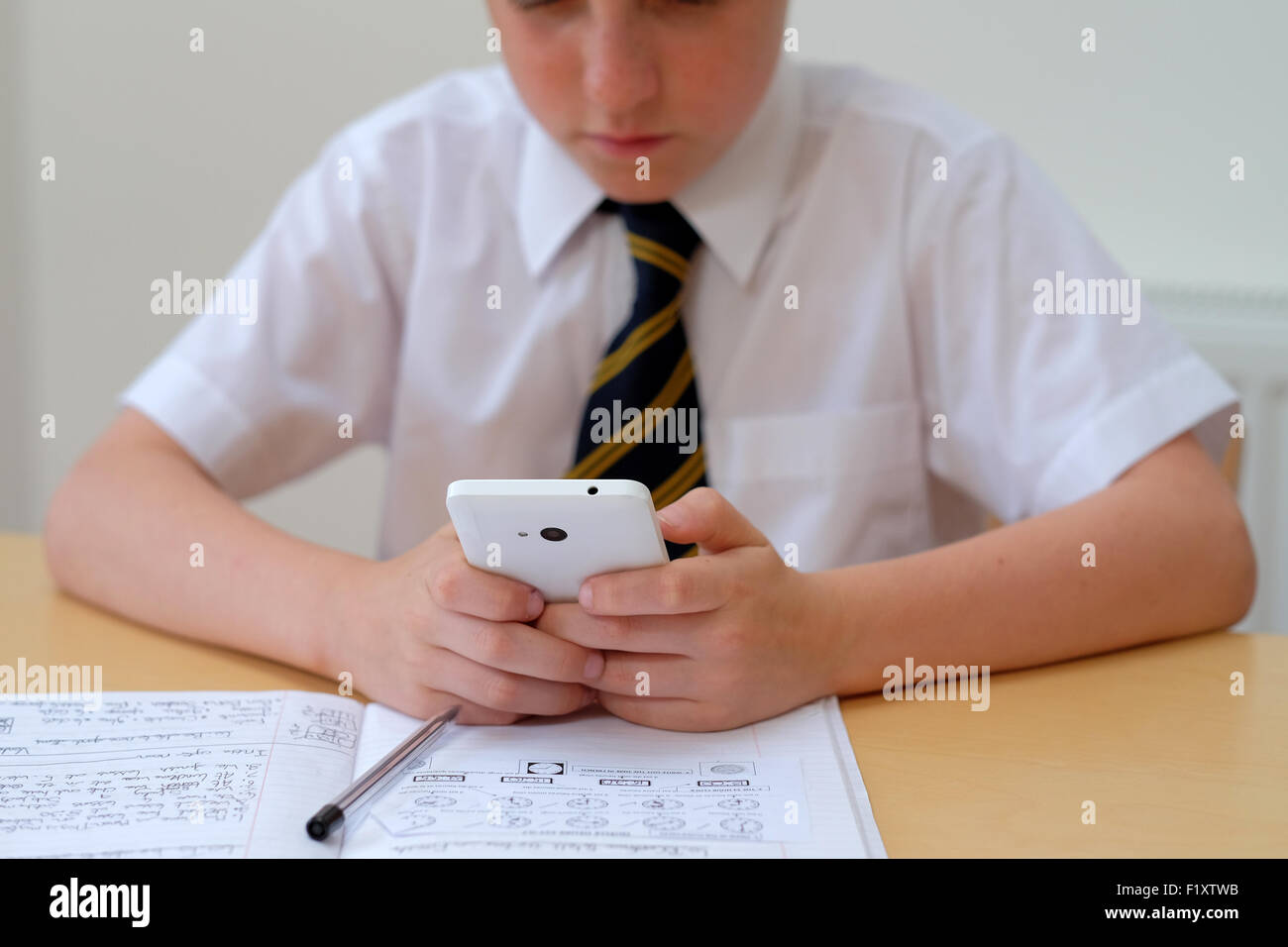 Schüler/abgelenkt durch mit einem Mobiltelefon (SMS), während an seinem Schreibtisch saß mit seinem Kurs arbeiten zu Hause aus arbeiten Stockfoto
