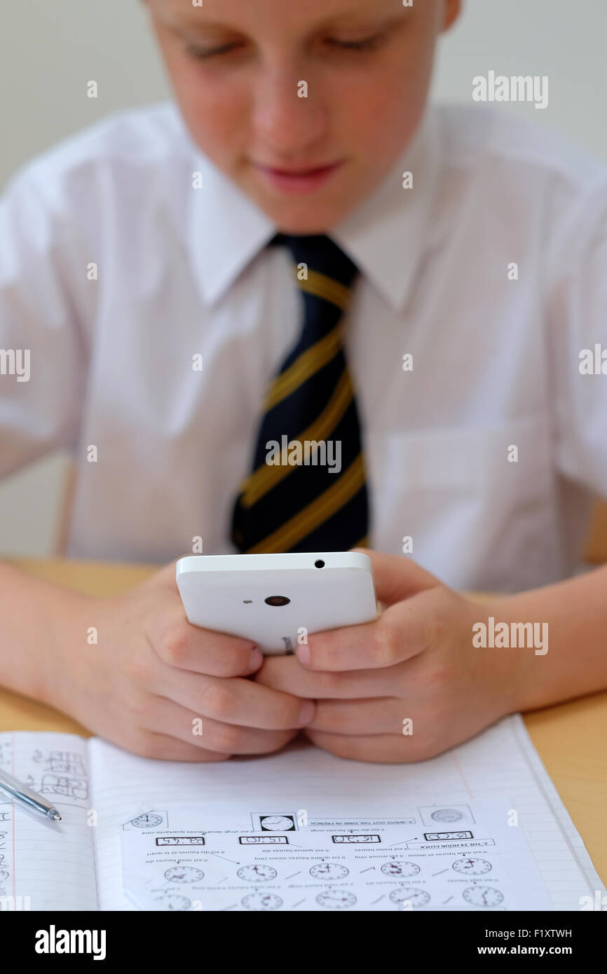 Schüler/abgelenkt durch mit einem Mobiltelefon (SMS), während an seinem Schreibtisch saß mit seinem Kurs arbeiten zu Hause aus arbeiten Stockfoto