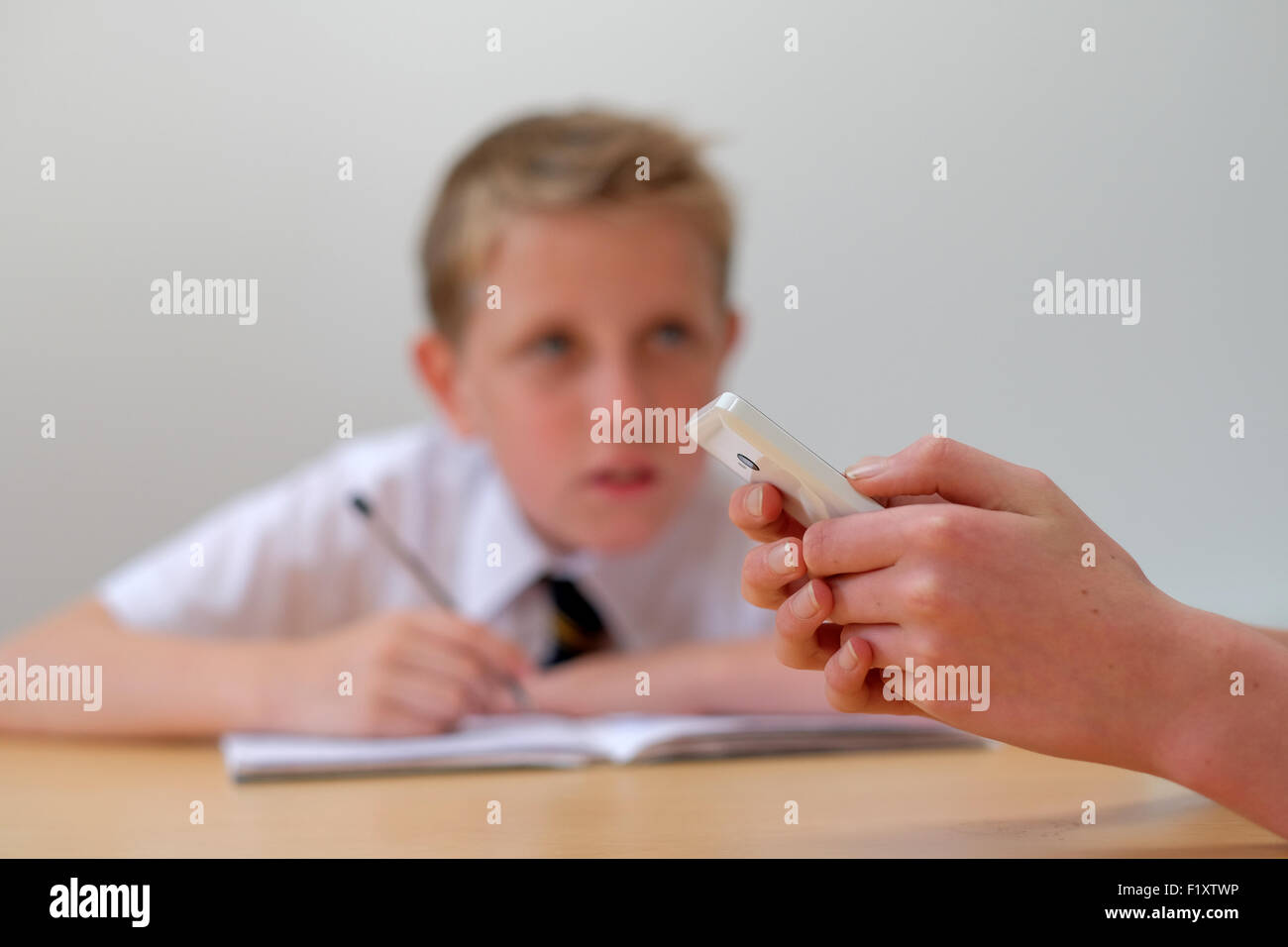 Ein Schüler mit einem Mobiltelefon (SMS) in der Klasse wie ein weiterer Schüler im Hintergrund arbeitet Stockfoto