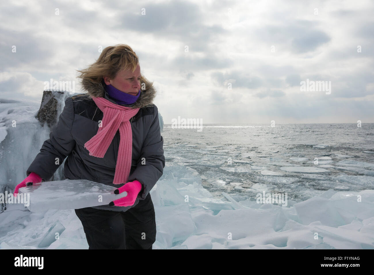 Blonde Frau kaukasischen in ihren 40ern trägt einen Wintermantel und rosa Schal bereitet sich auf ein großes Stück der Platte Eis am Ufer werfen Stockfoto