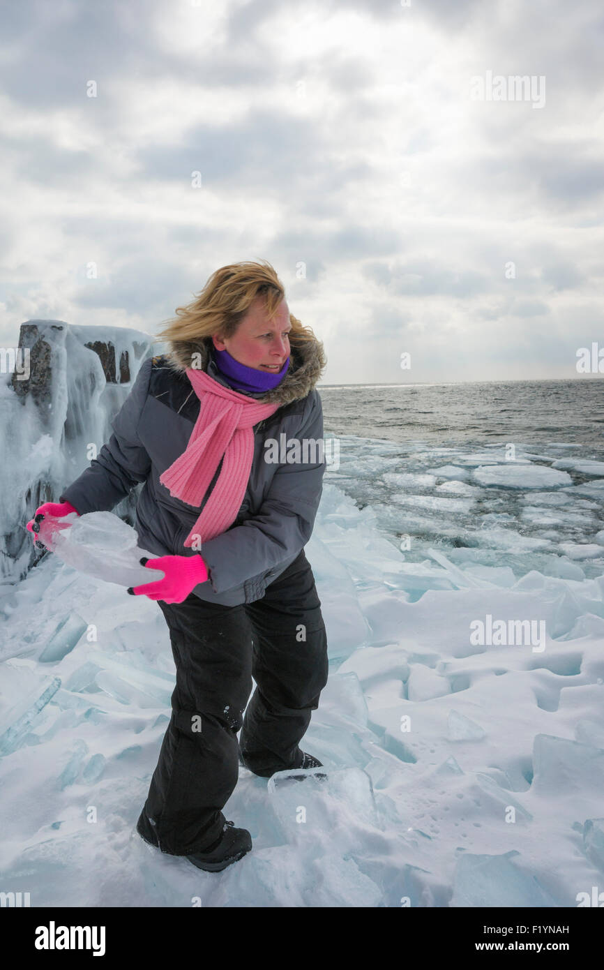 Blonde Frau wirft Eisbrocken von gefrorenen Ufer am Lake Superior im Norden von Minnesota an einem Wintertag Stockfoto