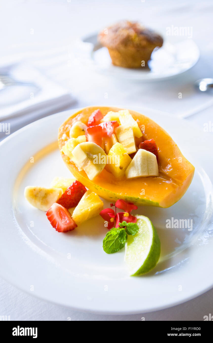 Frühstück Obstsalat auf einem klaren weißen Teller auf eine weiße Tischdecke mit einem Muffin im Hintergrund Stockfoto