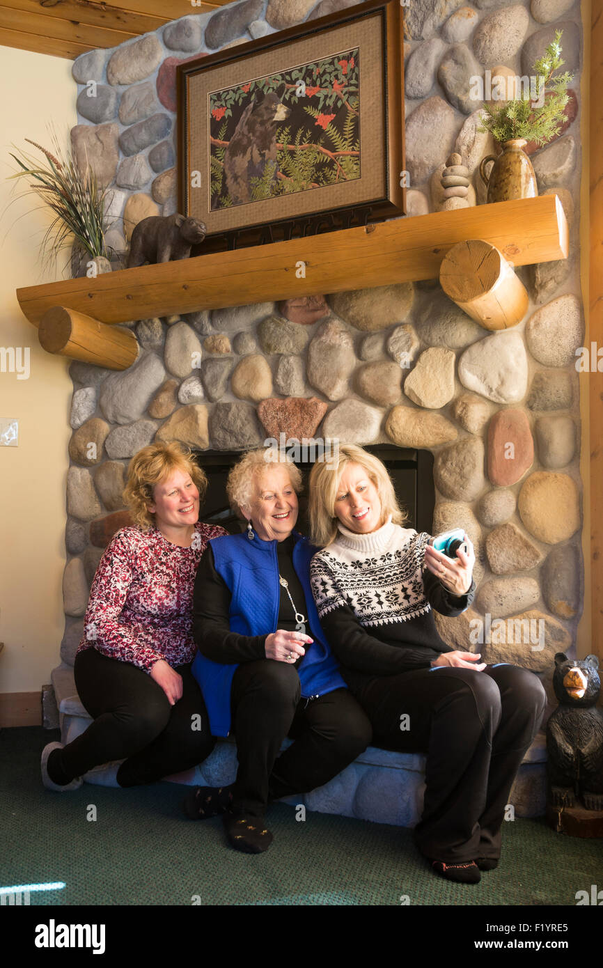 Drei glückliche Blondine kaukasischen Frauen sitzen auf einem Kamin Felsvorsprung lächelnd in die Kamera, ein Selbstporträt in den Urlaub nehmen Stockfoto