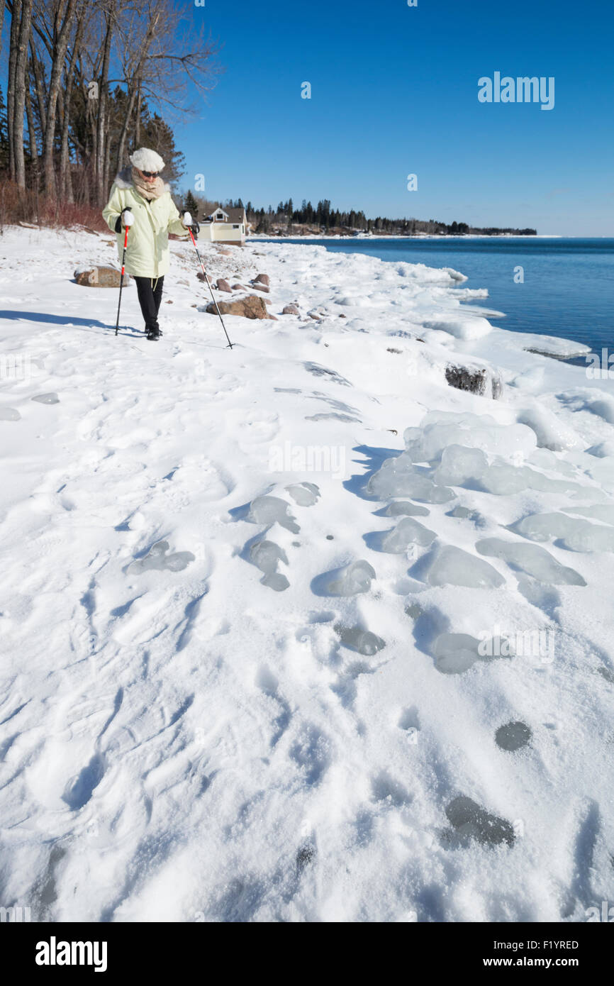 Ältere Frau in 70er Jahren geht über die eisigen ungleichmäßige gefrorenen Ufer des Lake Superior im Winter, zwei Häfen, MN, USA Stockfoto