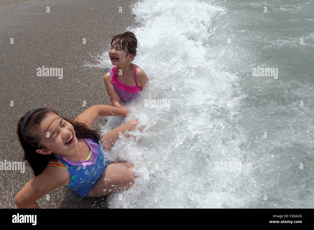 Kinder spielen im Wasser mit den Wellen am Strand Stockfoto