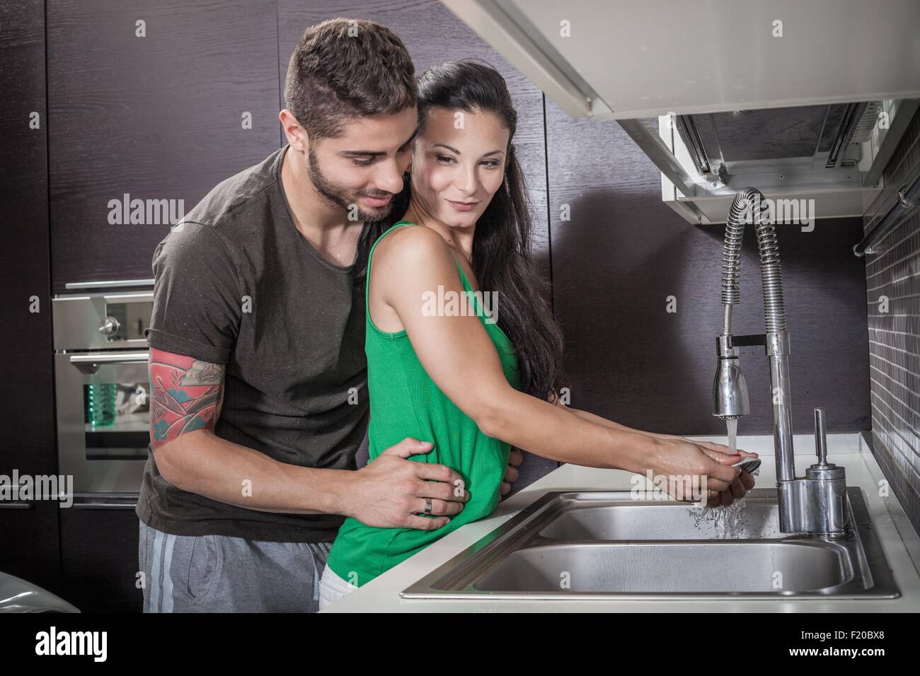 Junge Frau, Abwasch, während von Freund umarmt Stockfoto