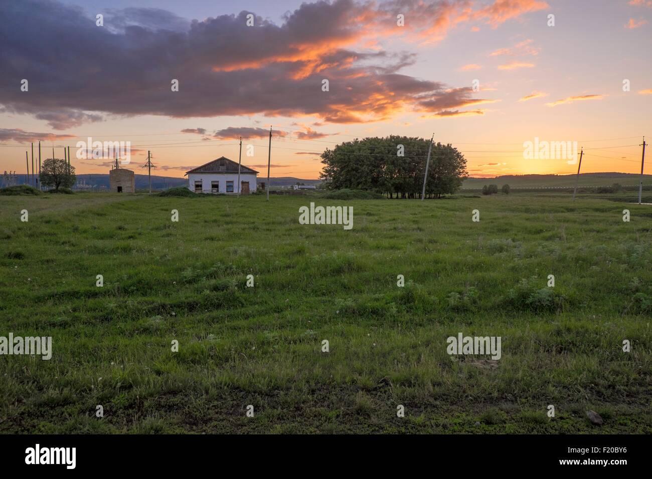 Blick auf den Sonnenuntergang des Feldes mit entfernten ländlichen Haus Stockfoto