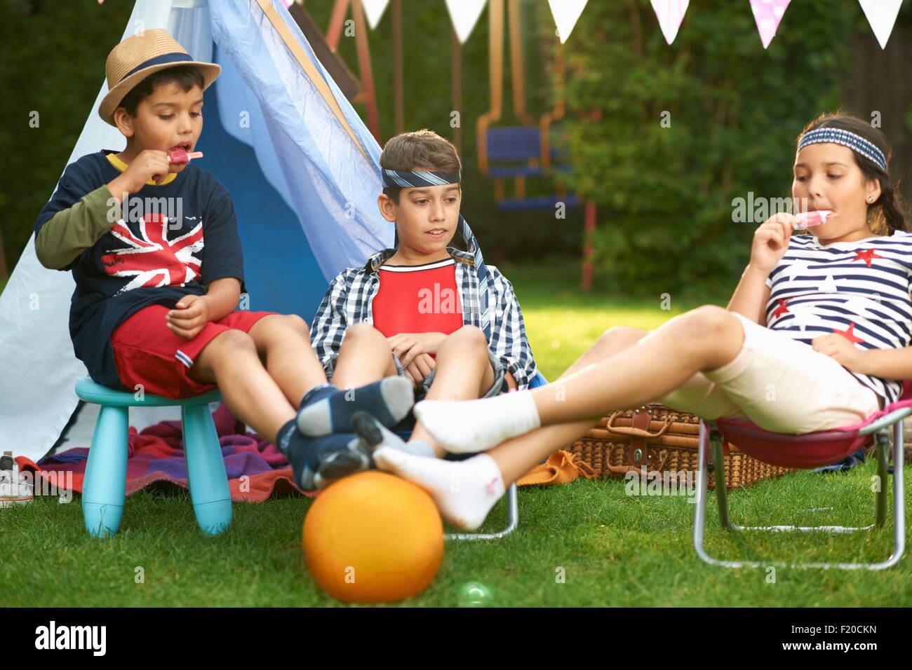 Mädchen und Brüder essen Eis am Stiehl vor hausgemachten Zelt im Garten Stockfoto Mädchen und Brüder essen Eis am Stiehl vor hausgemachten Zelt im Garten Stockfoto