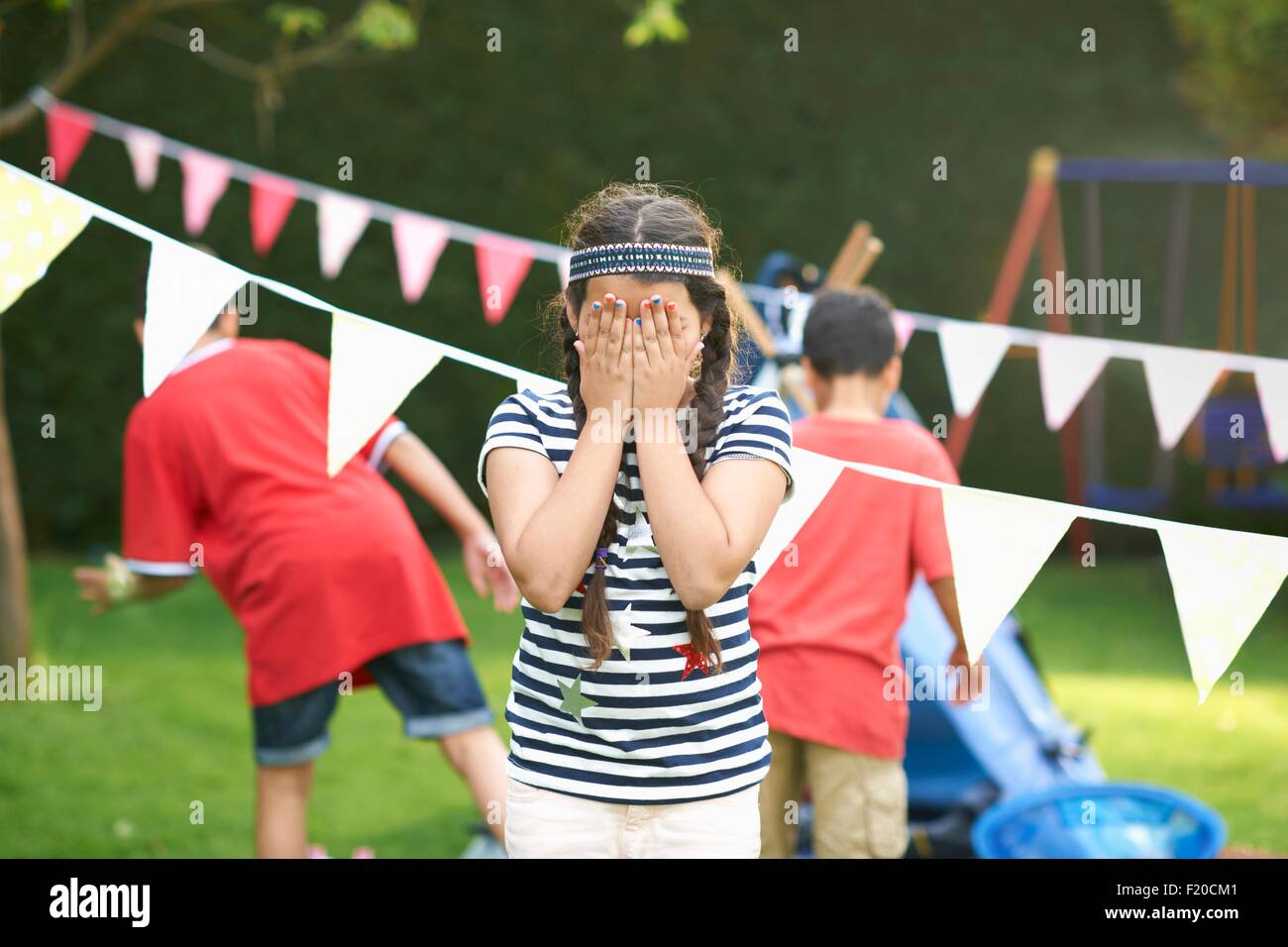 Mädchen über ihr Augen für Hide and seek mit Brüder im Garten Stockfoto