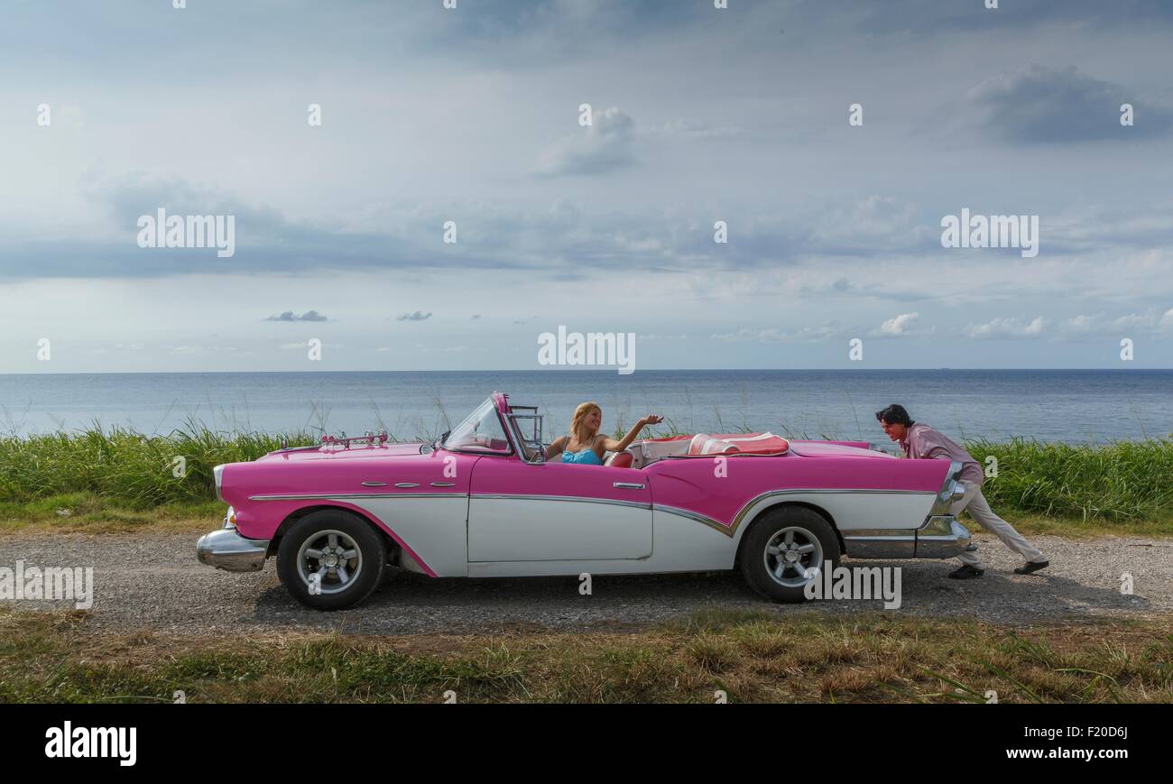 Junger Mann schob Oldtimer Cabrio an Küste, während Freundin, Havanna, Kuba treibt Stockfoto