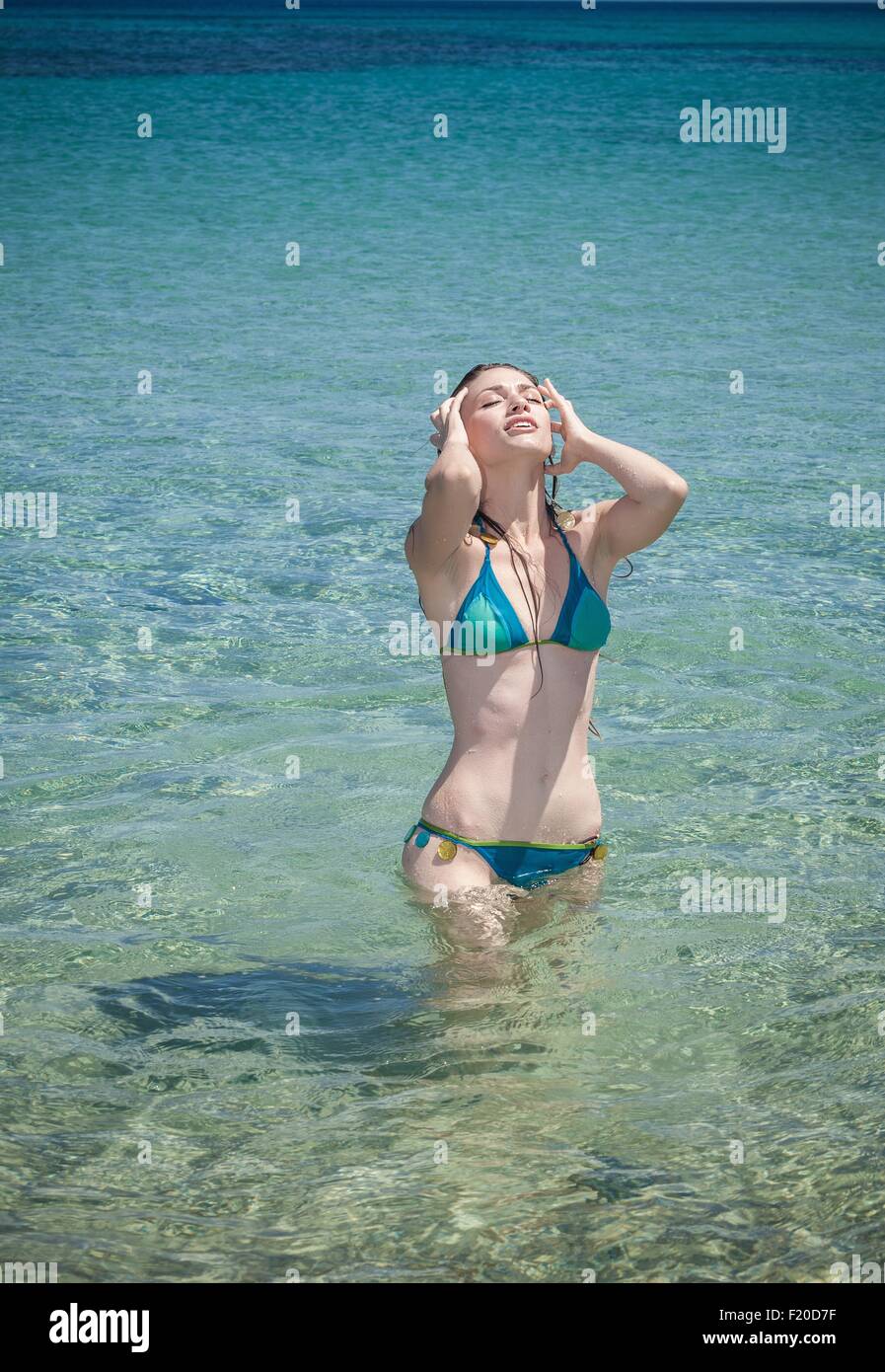 Junge Frau trägt Bikini mit Händen in Haaren im Meer, Cagliari, Sardinien, Italien Stockfoto