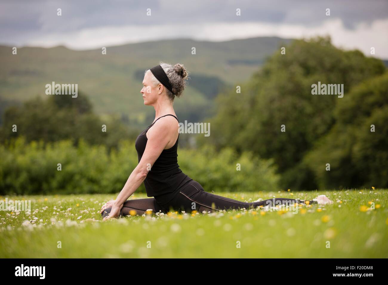 Reife Frau dabei spaltet praktizieren Yogaposition im Feld Stockfoto
