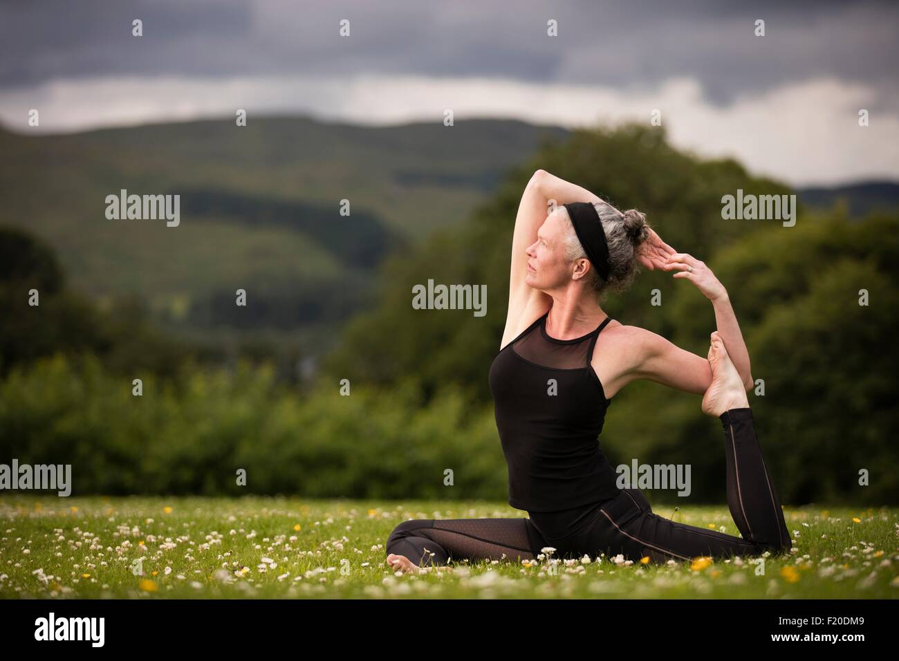 Reife Frau dabei spaltet Yoga zu praktizieren im Feld Stockfoto