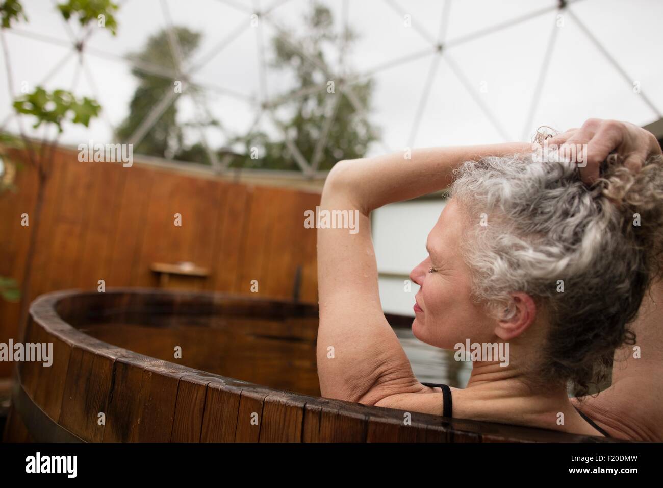 Reife Frau mit Händen in Haaren im Whirlpool bei Eco retreat Stockfoto