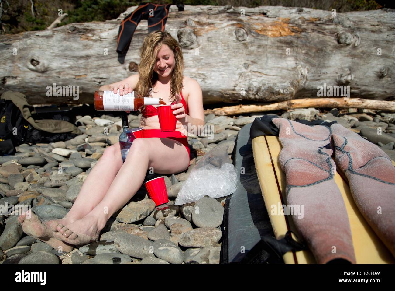 Junge Frau sitzt am felsigen Strand, Gießen Getränk, Short Sands Beach, Oregon, USA Stockfoto Junge Frau sitzt am felsigen Strand, Gießen Getränk, Short Sands Beach, Oregon, USA Stockfoto