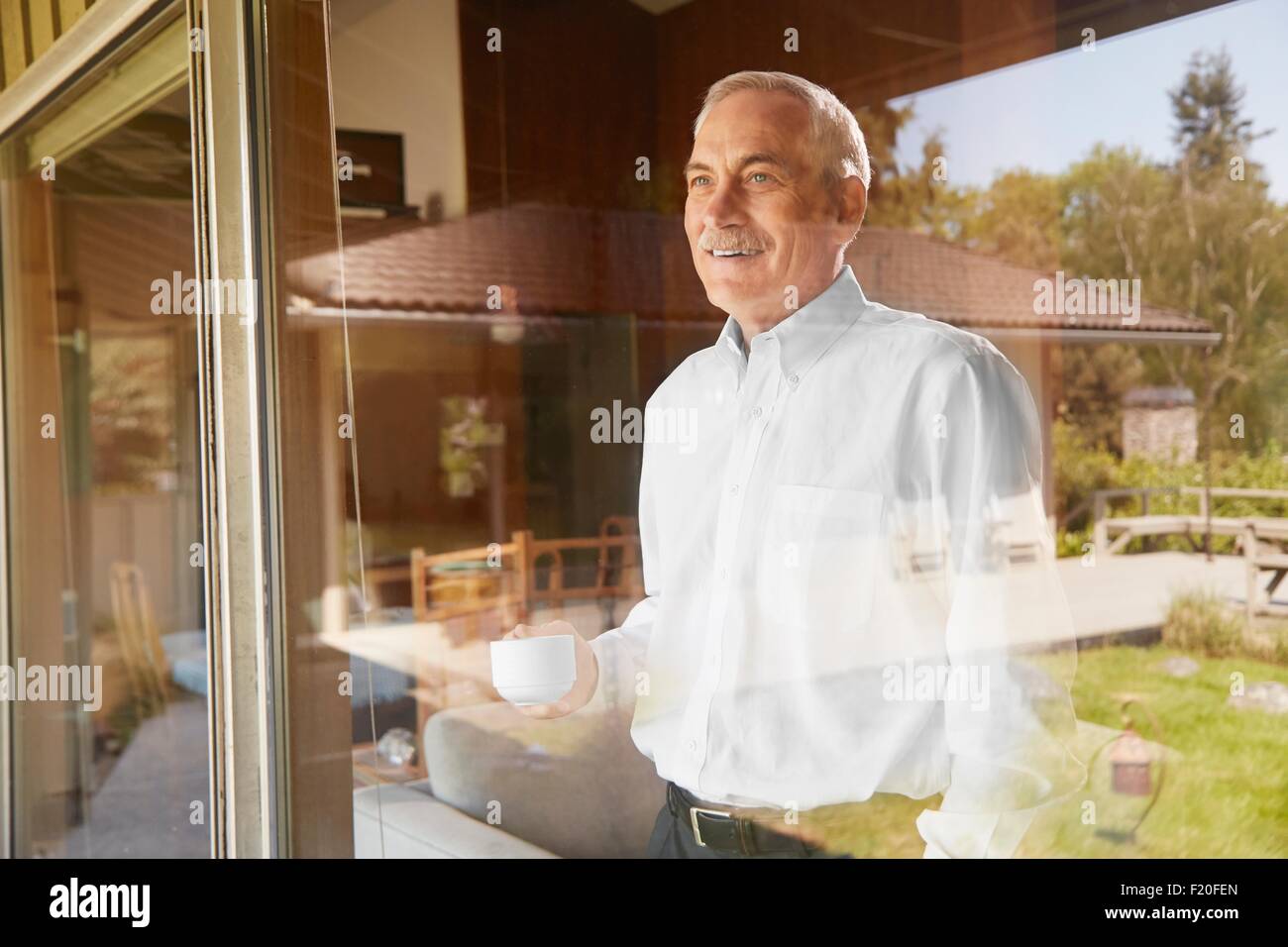 Ältere Mann zu Hause Kaffee trinken, Blick aus Fenster Stockfoto