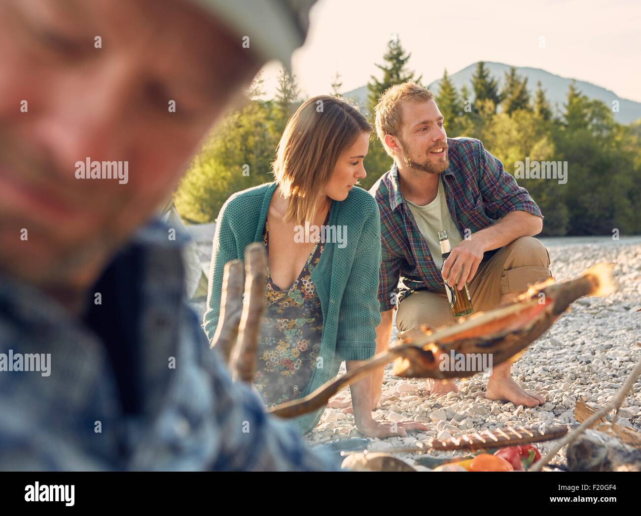Junges Paar neben Lagerfeuer Kochen Fisch, wegschauen Stockfoto