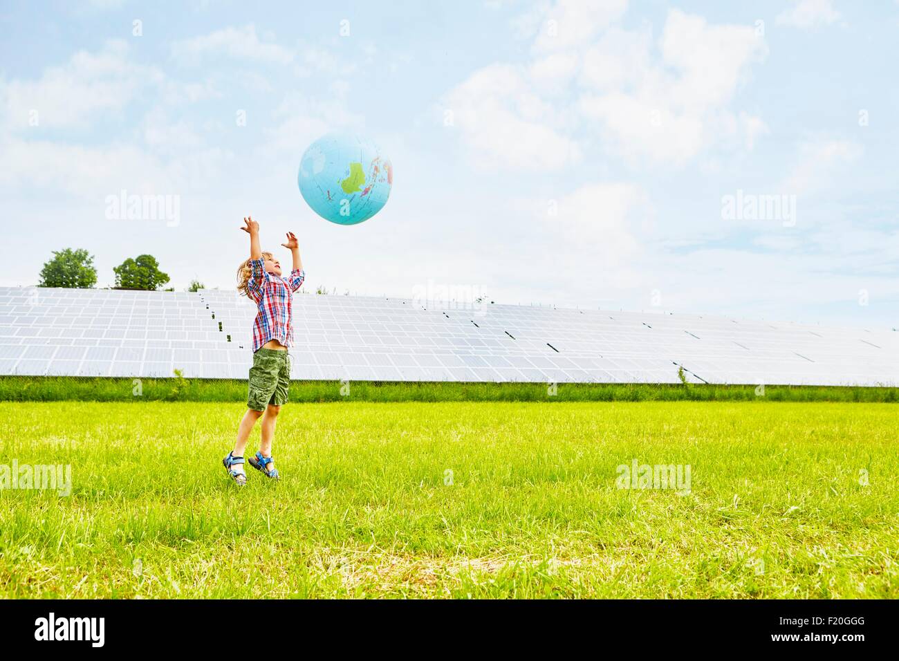 Kleiner Junge spielt mit aufblasbaren Ball auf Feld neben Solarpark Stockfoto