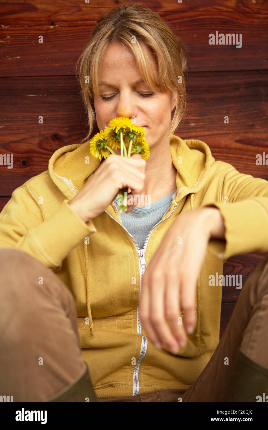 Reife Frau sitzen Holzhütte, gelbe Blumen riechen Stockfoto