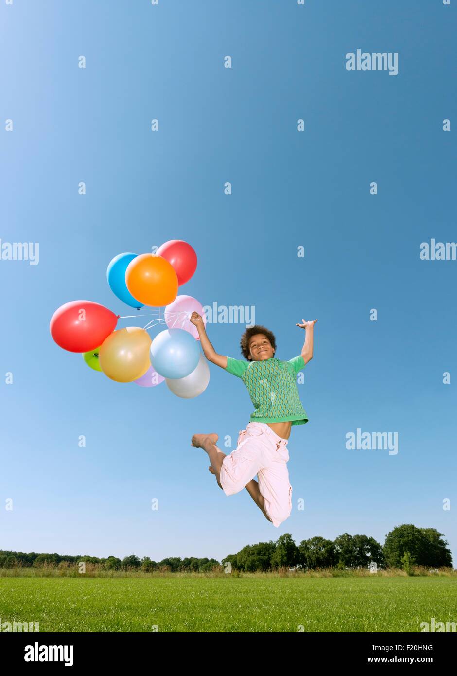 Junge hält Haufen Luftballons springen Luft gegen blauen Himmel Stockfoto