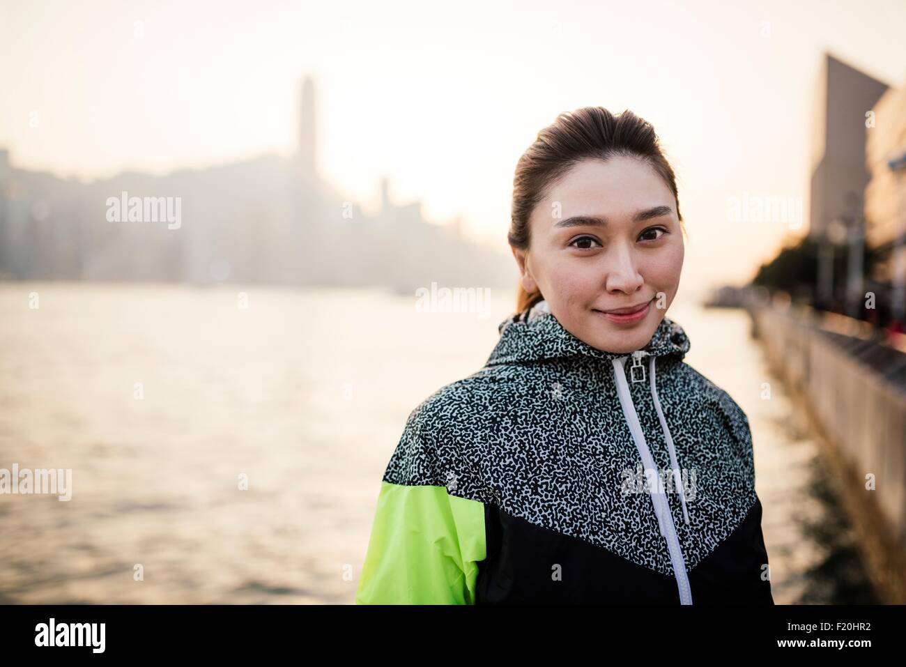 Porträt der jungen Frau trägt Trainingsjacke vor Wasser lächelnd Stockfoto