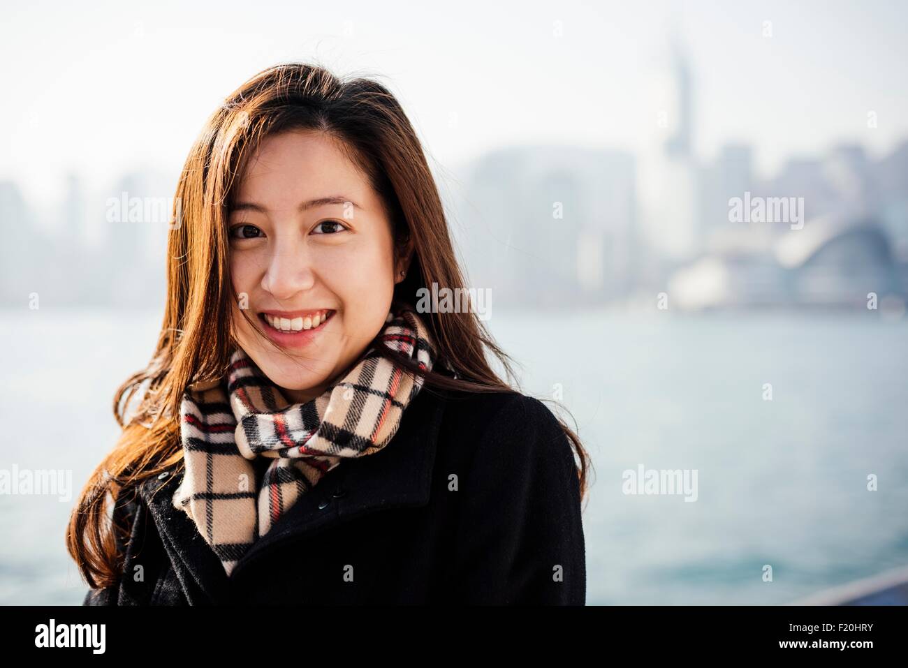 Porträt der jungen Frau mit überprüft Schal vor Wasser, Blick auf die Kamera zu Lächeln Stockfoto