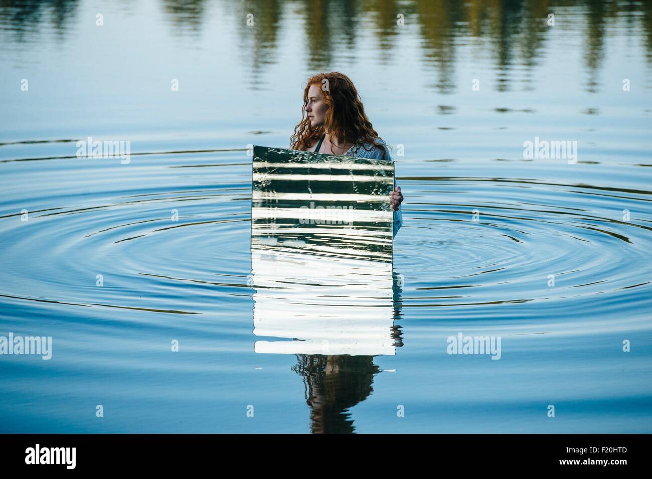 Junge Frau im See, Holding-Spiegel, Wasser plätschert in Spiegel reflektieren Stockfoto