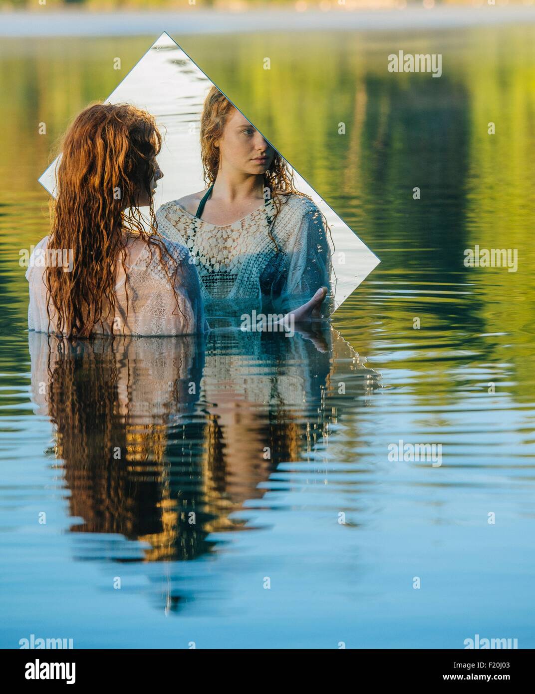 Junge Frau im See stehend, Spiegel, Spiegelbild betrachten Stockfoto