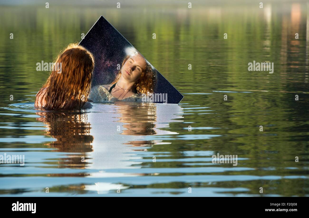 Junge Frau im See stehend, Spiegel, Spiegelbild betrachten Stockfoto