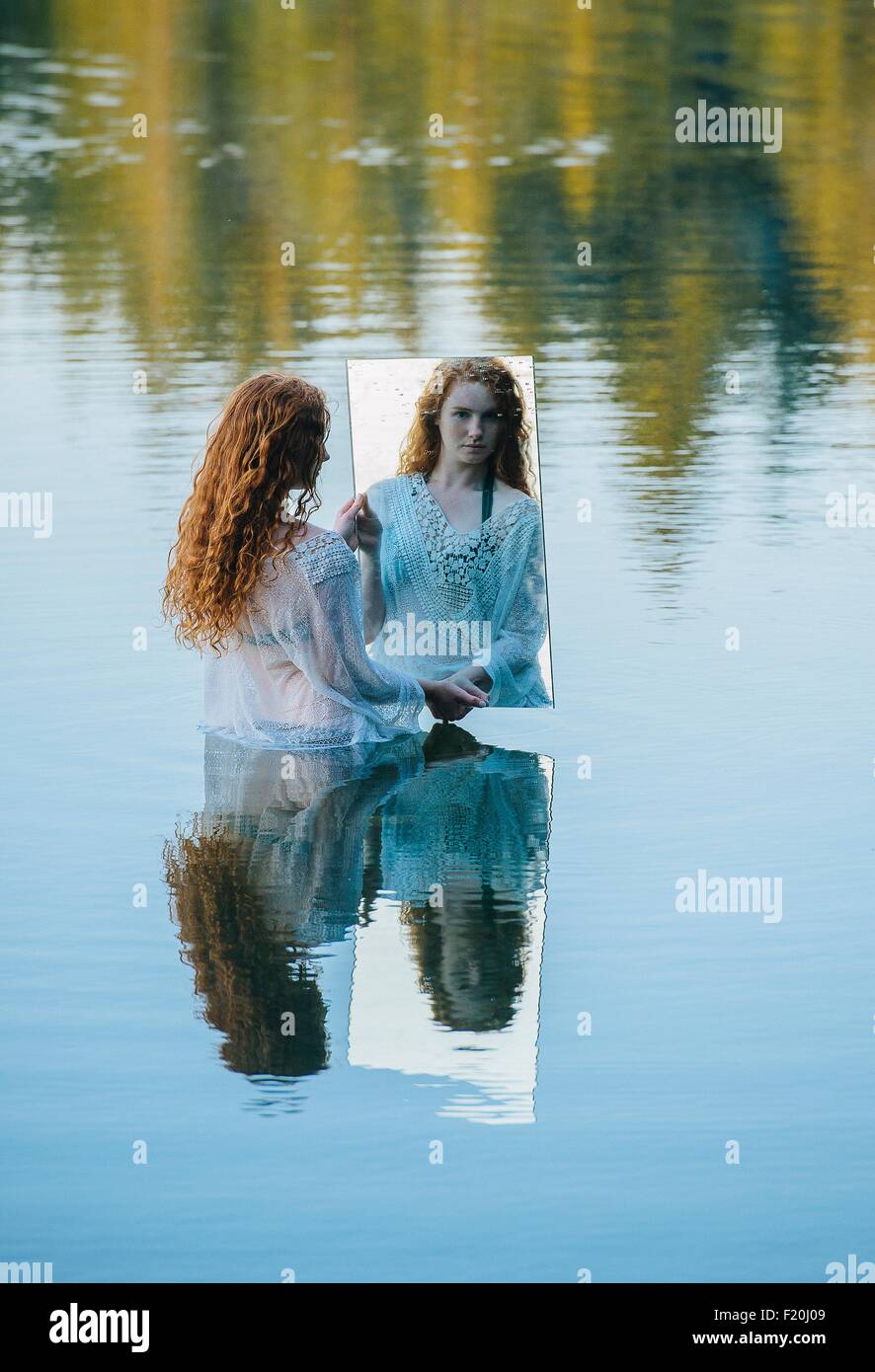 Junge Frau im See stehend, Spiegel, Spiegelbild betrachten Stockfoto