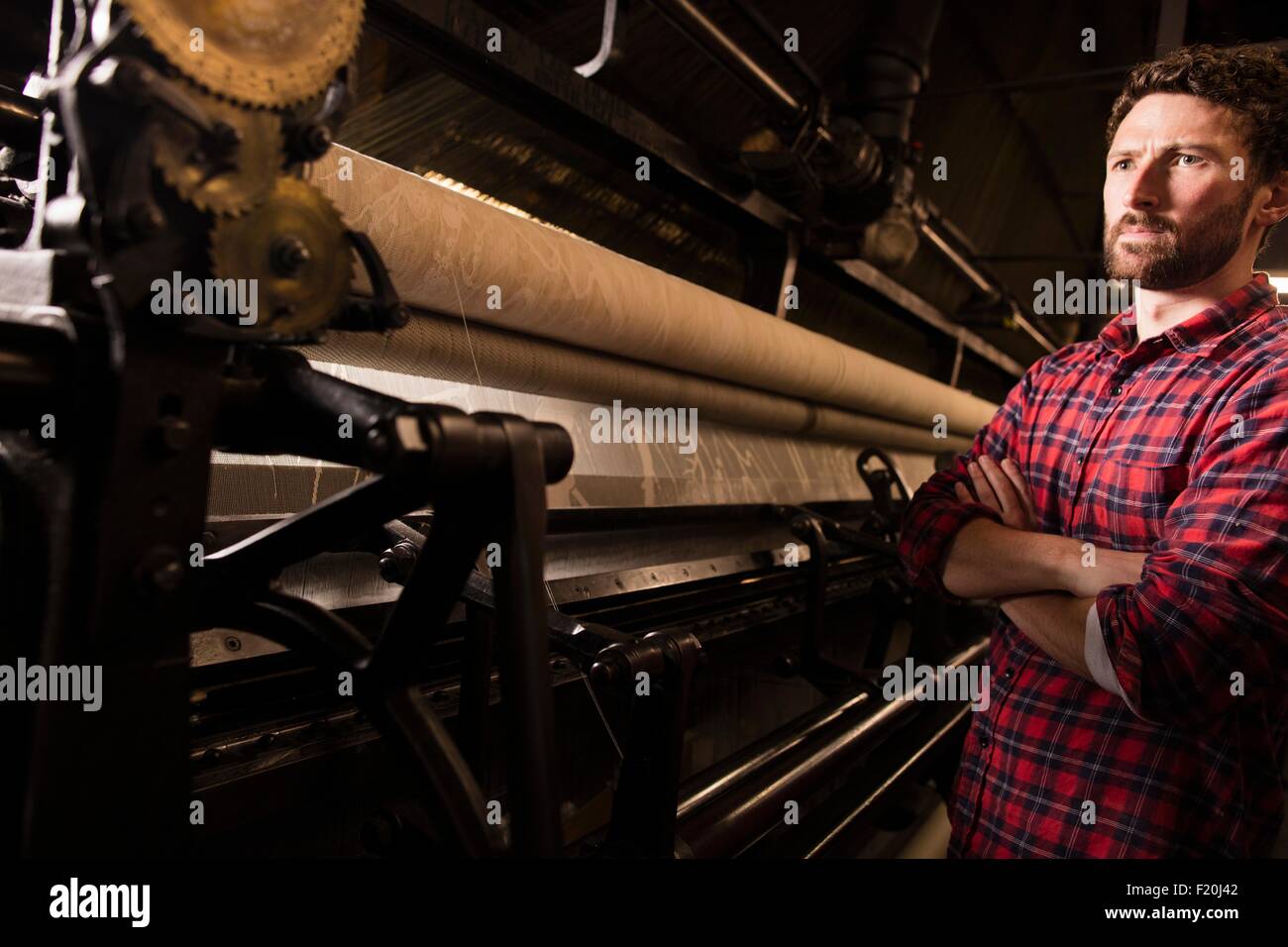 Porträt des jungen männlichen Weaver und alten Webmaschine in Textilfabrik Stockfoto