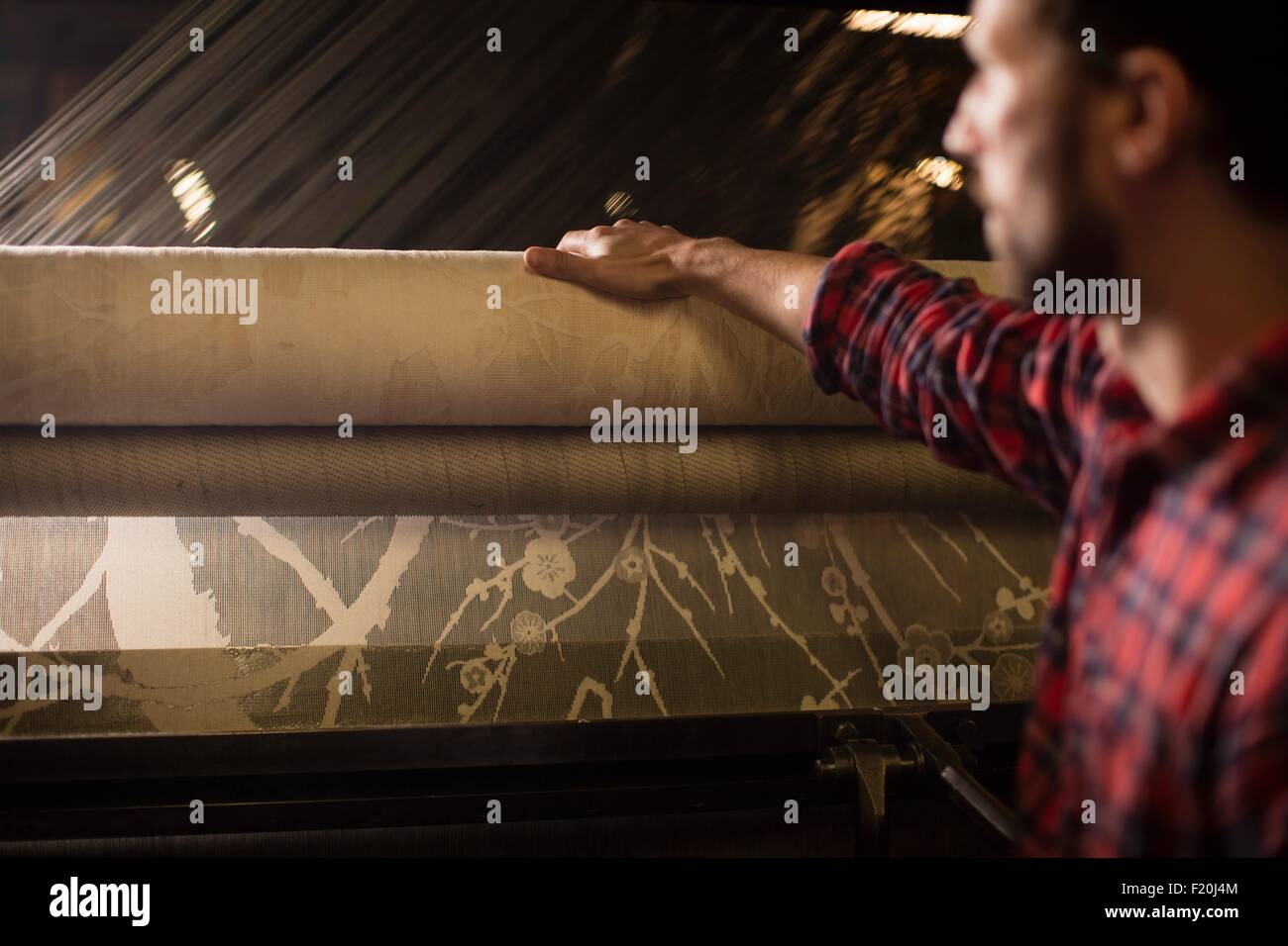 Junge männliche Weberin mit Spitze Rollen auf alten Webmaschine in Textilfabrik Stockfoto