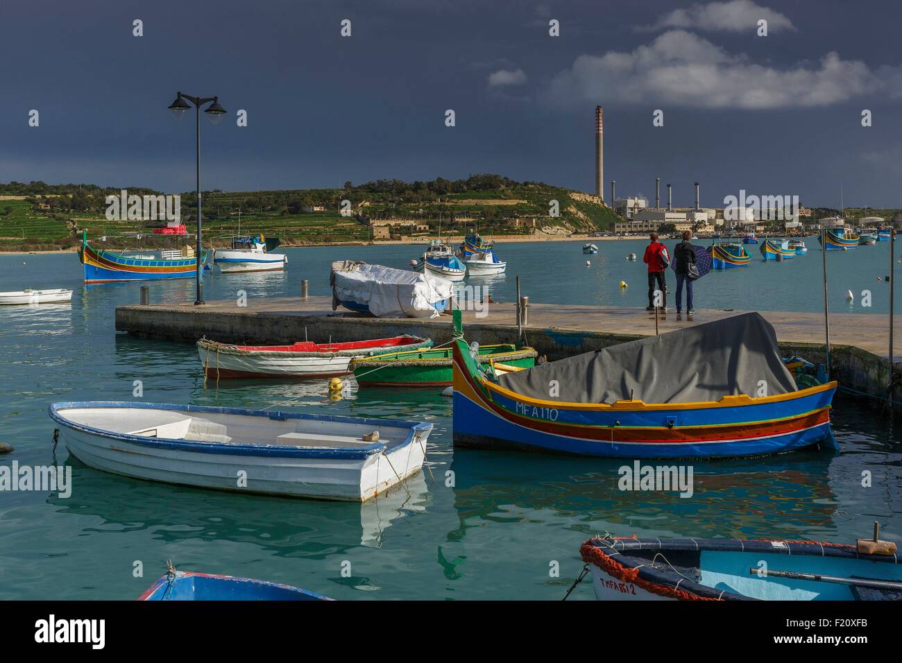 Malta, Marsaxlokk, Zuschauer zu Fuß auf den Docks des Fischerdorfes bei bewölktem Himmel Stockfoto