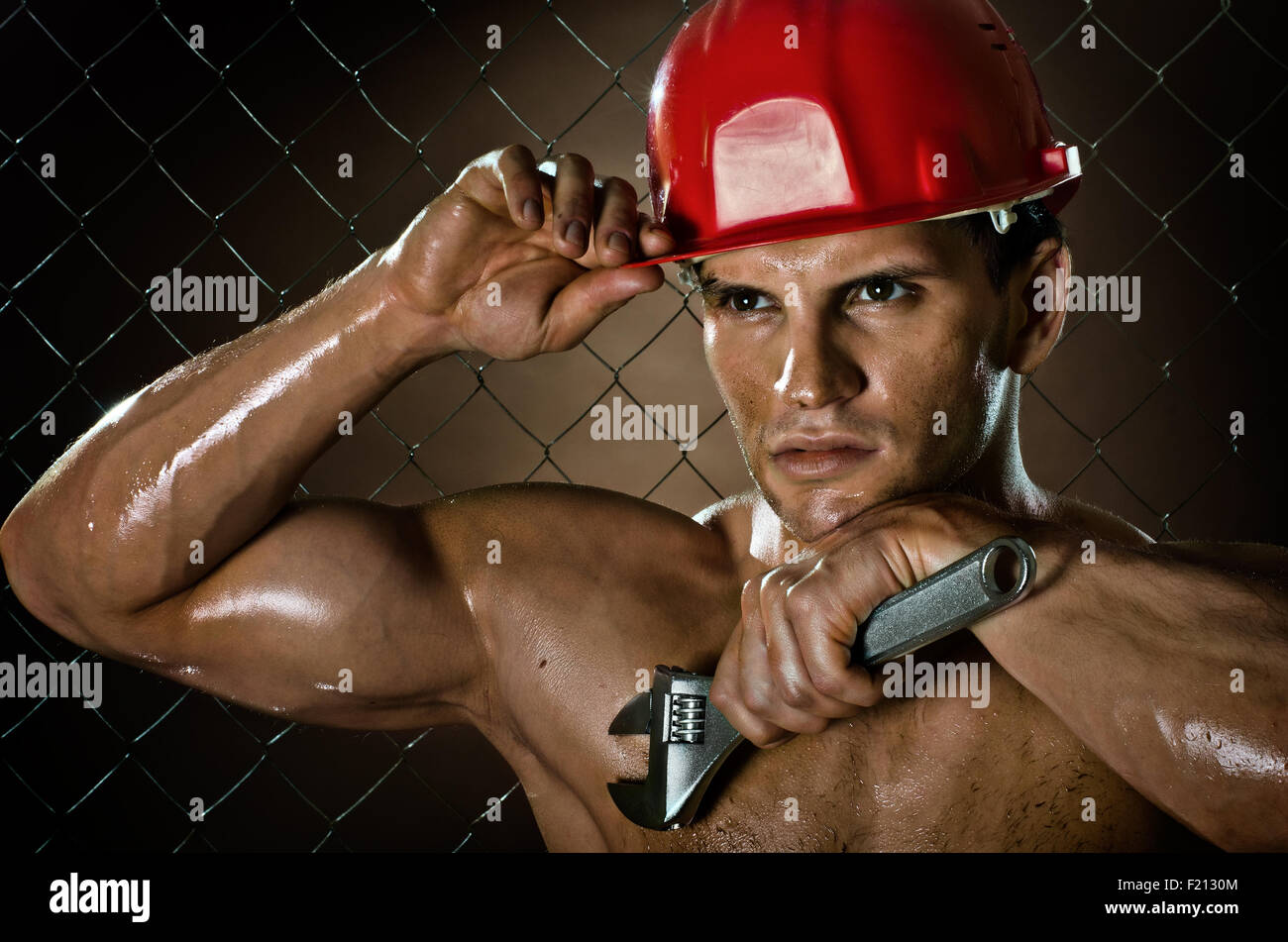Closeup Portrait der Schönheit muskulösen Arbeiter im roten Schutzhelm mit großen verstellbaren Schraubenschlüssel in der hand, schmutzigen und verschwitzt Stockfoto