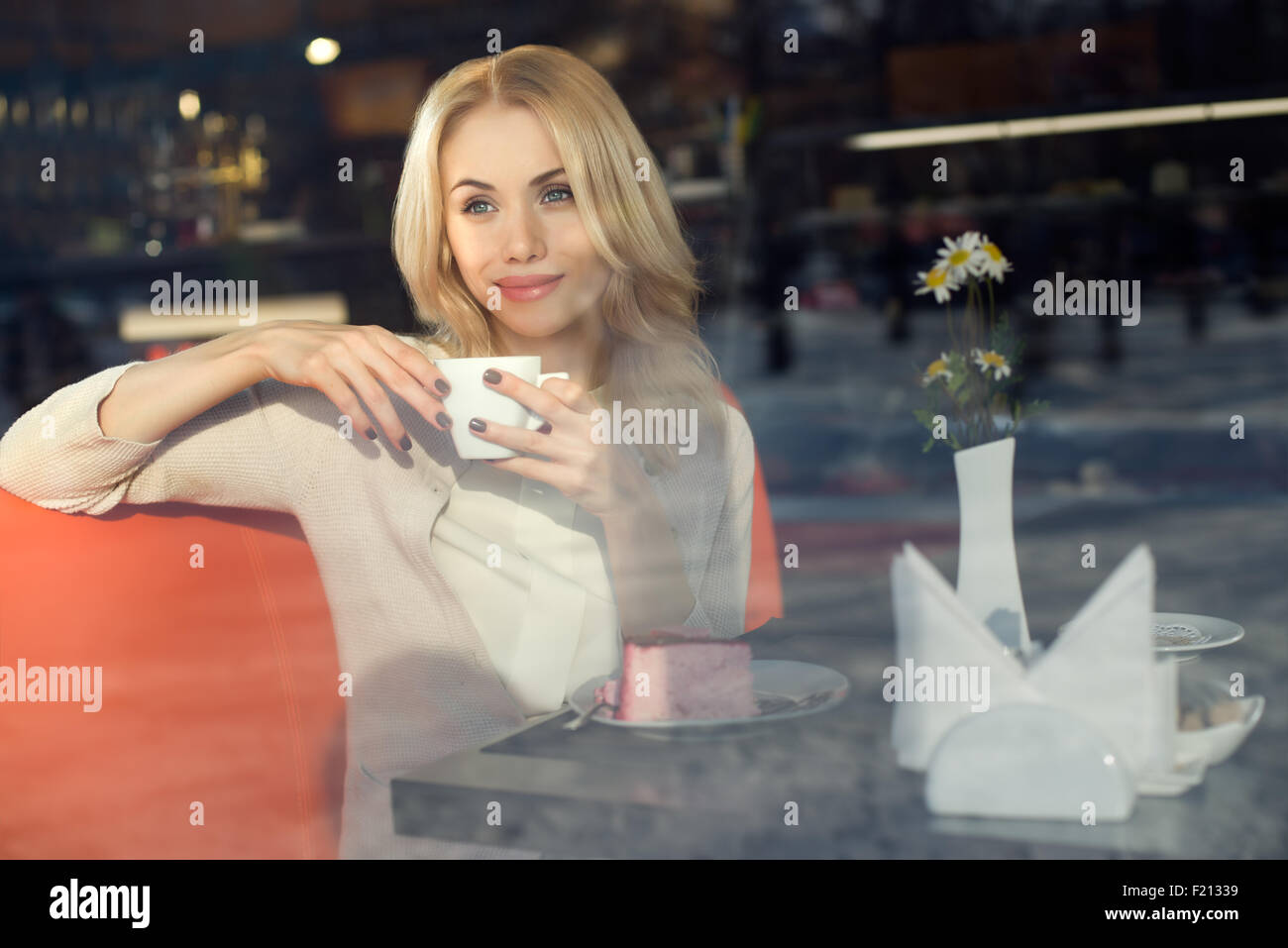 Sitzen Sie sehr schöne junge Frau, im Cafe und trinken Kaffee oder Tee, Croissant, Straße Frontscheibe Ansicht Stockfoto