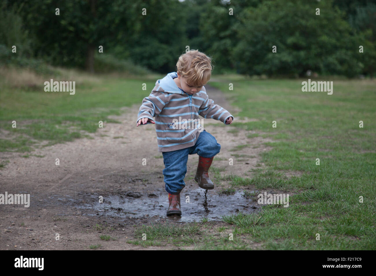 20 Monate Alter jungen genießt treten in einer schlammigen Pfütze nach einer Anzahl von Regentagen und Herbstwetter, Wimbledon Common, London Stockfoto