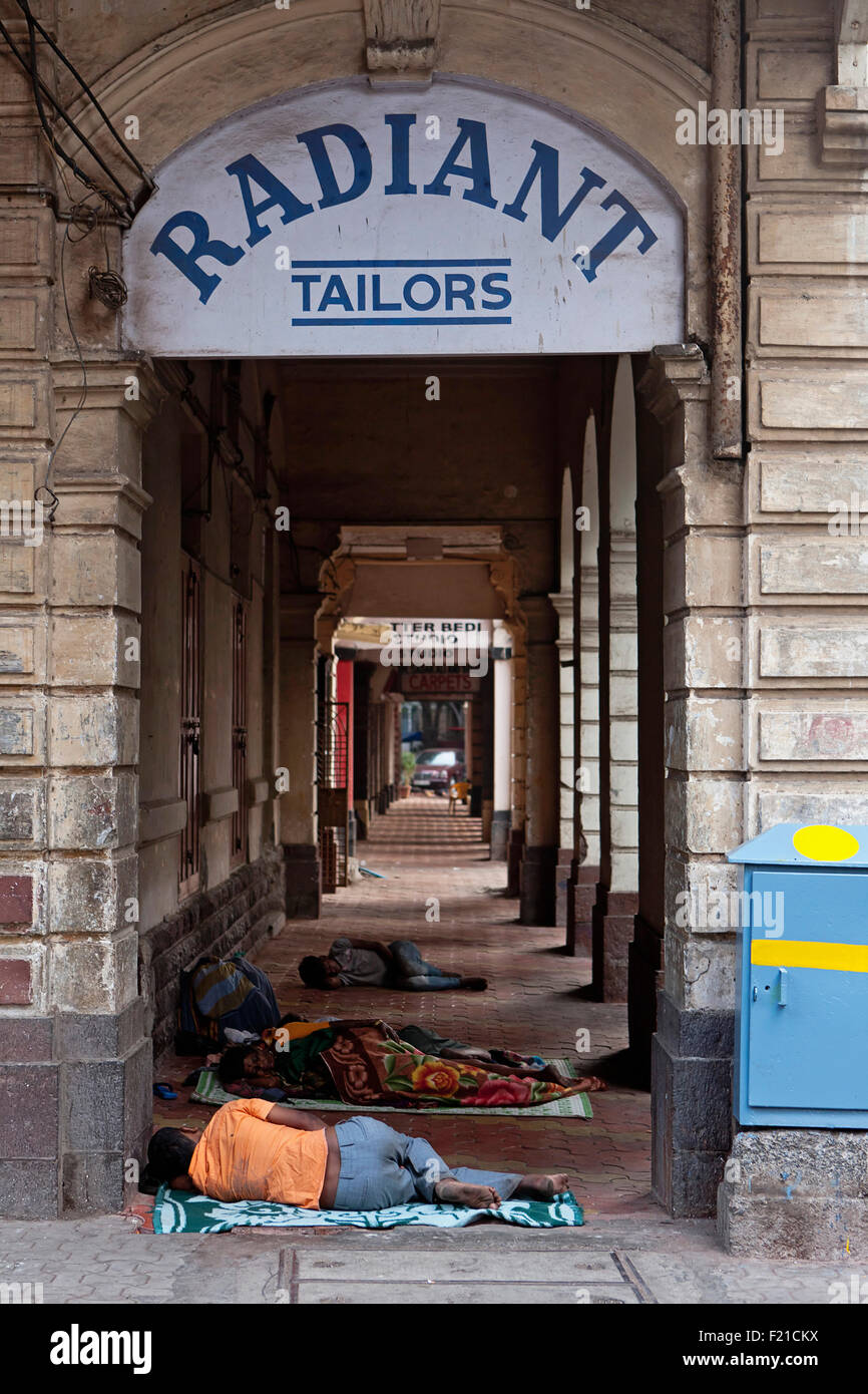 Indien Maharashtra Mumbai Obdachlose schlafen auf dem Bürgersteig in einer Arkade von Geschäften unter einem Schild mit der Aufschrift "Strahlende Schneider" Stockfoto