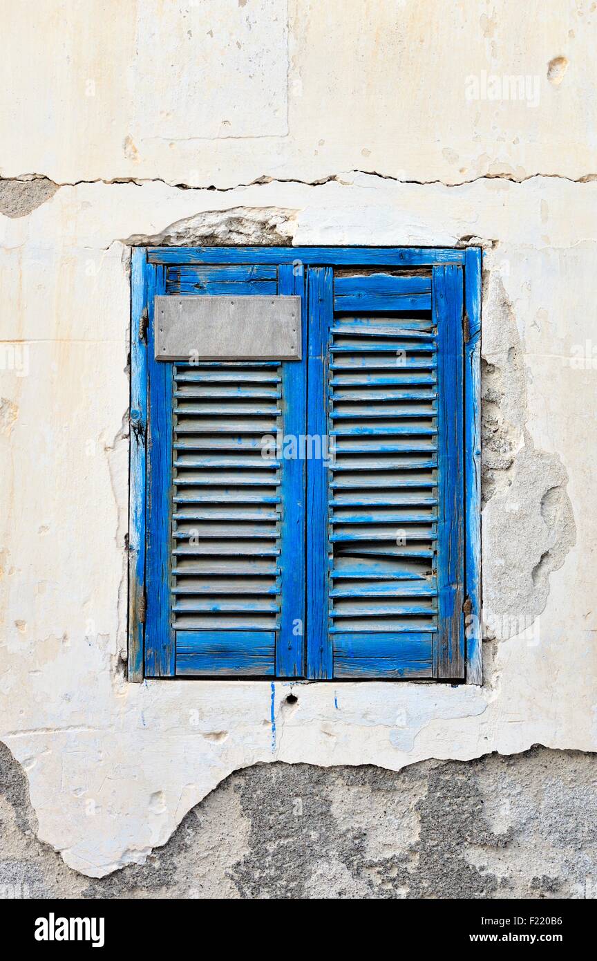 Eine abgenutzte blauen Fensterläden Fenster auf einem verfallenen Gebäude Außenwand Stockfoto