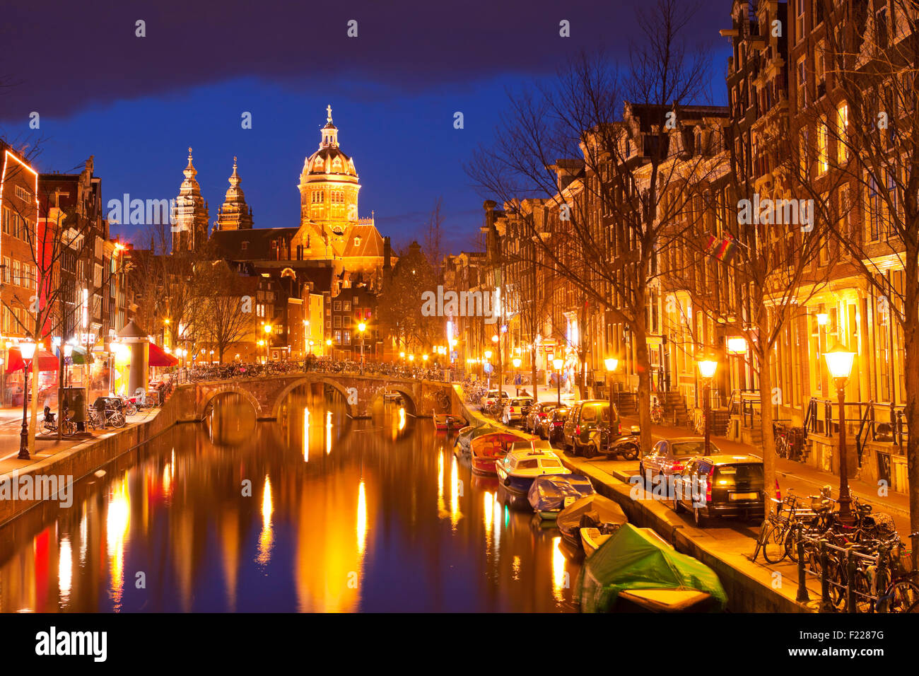 Ein Kanal im Rotlichtviertel in Amsterdam, Die Niederlande mit der St. Nikolaus Kirche am Ende fotografiert in der Nacht. Stockfoto