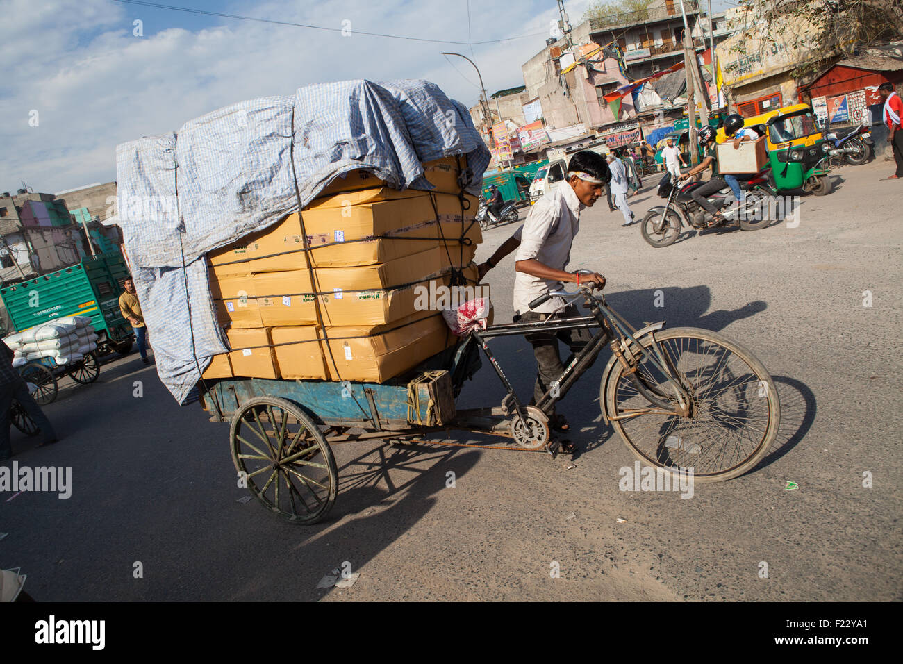Ein Mann schleppt eine schwere Last von Fracht auf einem Wagen auf der Rückseite von seinem Fahrrad durch die Straßen von Delhi Stockfoto