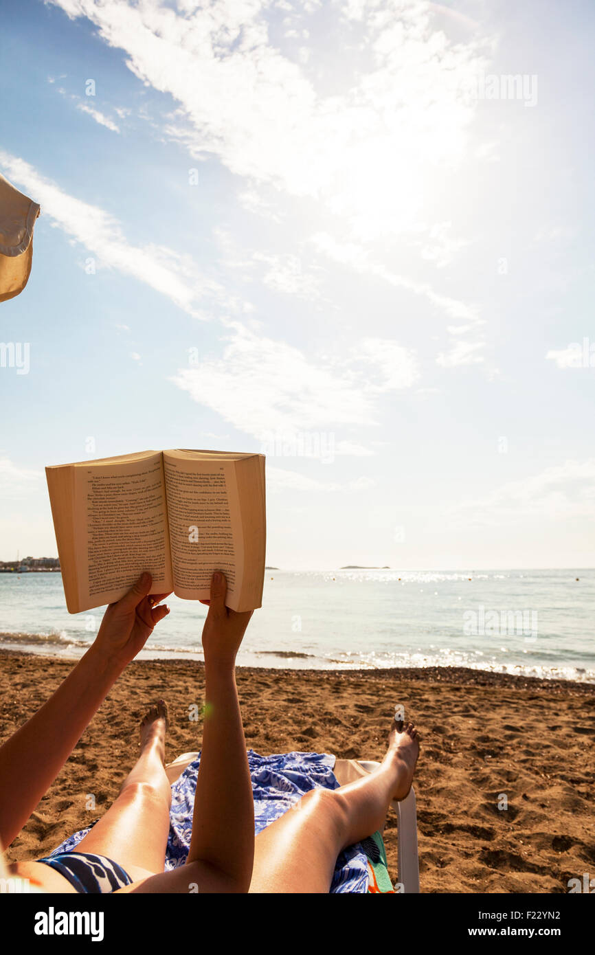 Buch auf Strandurlaub in Sonne Sonnenschein Frau Sonnenbaden gegen Himmel geöffneten Seiten lesen Stockfoto