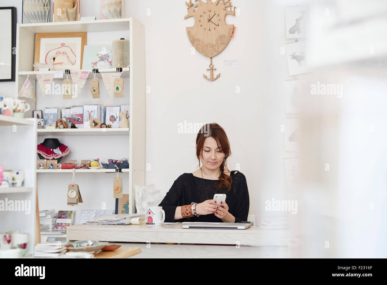 Eine ältere Frau sitzt mit einem Smartphone in einen Souvenirladen, einen kleinen Einzelhandel Geschäftsbetrieb. Stockfoto