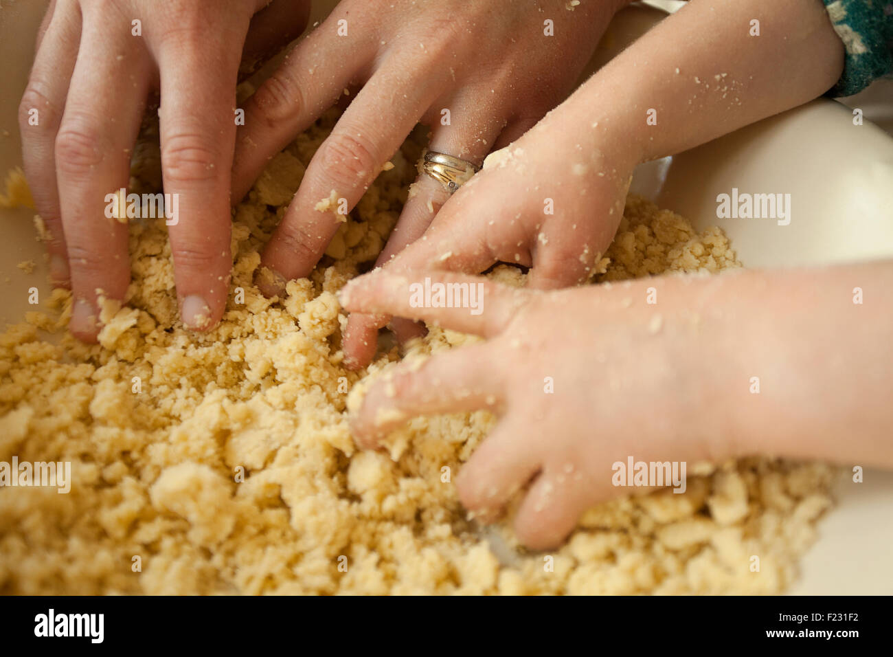 Zwei paar Hände mischen Zutaten in eine Schüssel, ein Erwachsener und ein Kind zusammen zu kochen. Stockfoto