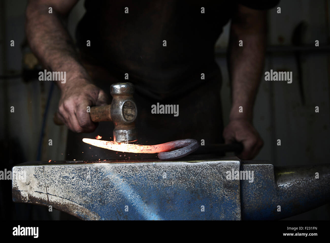 Ein Schmied, ein heißes Stück Eisen auf einem Amboss mit einem Hammer zu gestalten. Stockfoto
